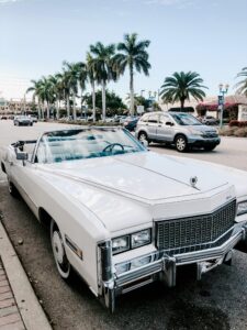 Classic white convertible parked under palm trees in a sunny street, capturing vintage automotive charm.